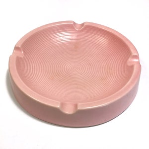 May include: A pink ceramic ashtray with a spiral design. The ashtray is round and has a wide, shallow bowl.