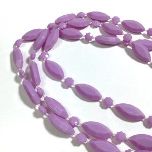 May include: A long strand of lavender-colored oval beads with smaller flower-shaped beads interspersed throughout.