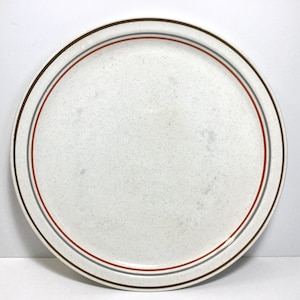 May include: Round, speckled white plate with a brown, gray, and red striped border. The plate has a simple, classic design, suitable for everyday use. The plate is made of ceramic.