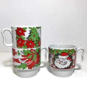 May include: White ceramic Christmas mugs with festive designs. One mug features a Santa Claus face, while others display poinsettias, a Christmas tree, and bells with red ribbons. Each mug has a unique handle.