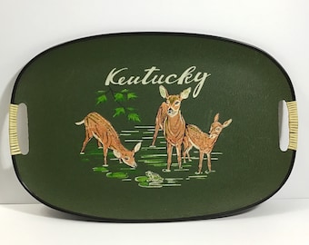 May include: A green oval serving tray with a black rim and woven handles. The tray features a painted scene of three deer in a forest setting with the word "Kentucky" in white lettering.