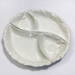 May include: White ceramic serving dish with four sections. The dish has a scalloped edge and a raised design.