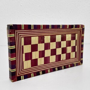 May include: A rectangular, handcrafted wooden box with a checkerboard pattern. The box features a red and natural wood checkerboard design, framed by red and white stripes. The edges are accented with purple, green, and black stripes.