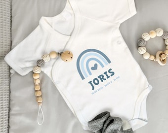 Könnte beinhalten: Ein weißer kurzärmeliger Babybody mit blauem Regenbogenmotiv, einem Herz, dem Namen JORIS sowie dem Text 10.09.2022, 3640 g, 51 cm. Der Body wird von einem Schnullerhalter aus Holzperlen und einem Paar grauer Socken ergänzt.