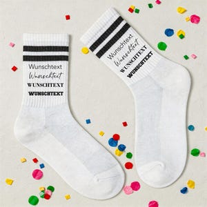 Könnte beinhalten: Ein Paar weiße Socken mit zwei schwarzen horizontalen Streifen am oberen Bündchen. Die Socken sind mit dem Text "Wunschtext" in vier verschiedenen Schriftarten und Stilen bedruckt, die sich vertikal an der Seite jeder Socke wiederholen.