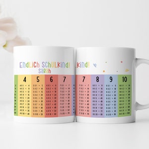 Könnte beinhalten: Zwei weiße Tassen mit einem Regenbogen-Design. Eine Tasse sagt "Endlich Schulkind! Sarah" und hat Multiplikationstabellen für 4, 5, 6 und 7. Die andere Tasse sagt "kind!" und hat Multiplikationstabellen für 7, 8, 9 und 10.
