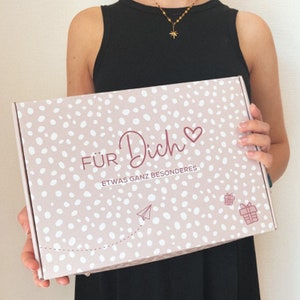 May include: A pink gift box with white polka dots and the words "F&Uuml;R Dich" and "ETWAS GANZ BESONDERES" in burgundy script. The box also features a heart, a paper airplane, and a gift icon.