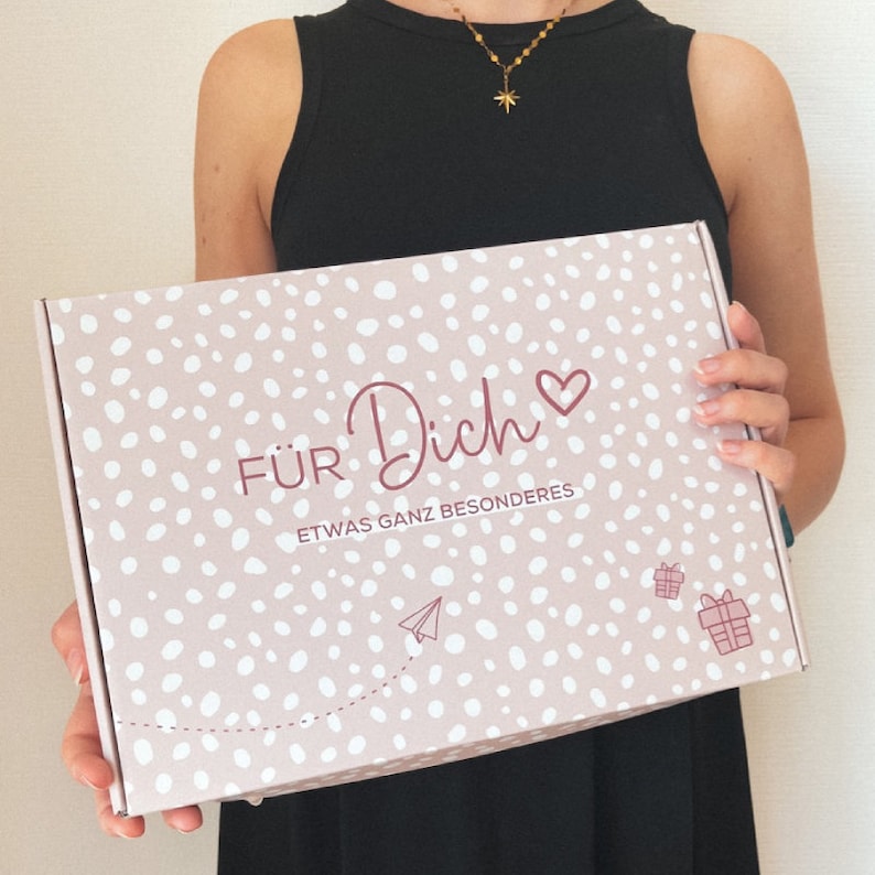 May include: A pink gift box with white polka dots and the words "F&Uuml;R Dich" and "ETWAS GANZ BESONDERES" in burgundy script. The box also features a heart, a paper airplane, and a gift icon.