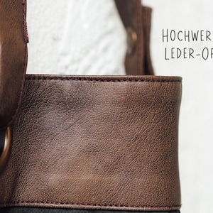 May include: Close-up of a brown tote bag with a textured leather-like appearance. The bag has dark brown handles and a metal ring detail. The text "HOCHWERTIGE LEDER-OPTIK" is visible on the right side.