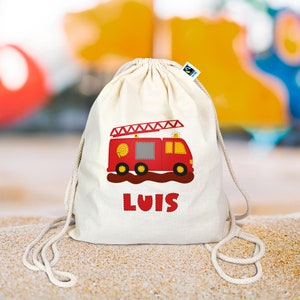 Può includere: Una borsa a cordoncino bianca con un design di camion dei pompieri rosso e il nome "LUIS" stampato sul davanti.