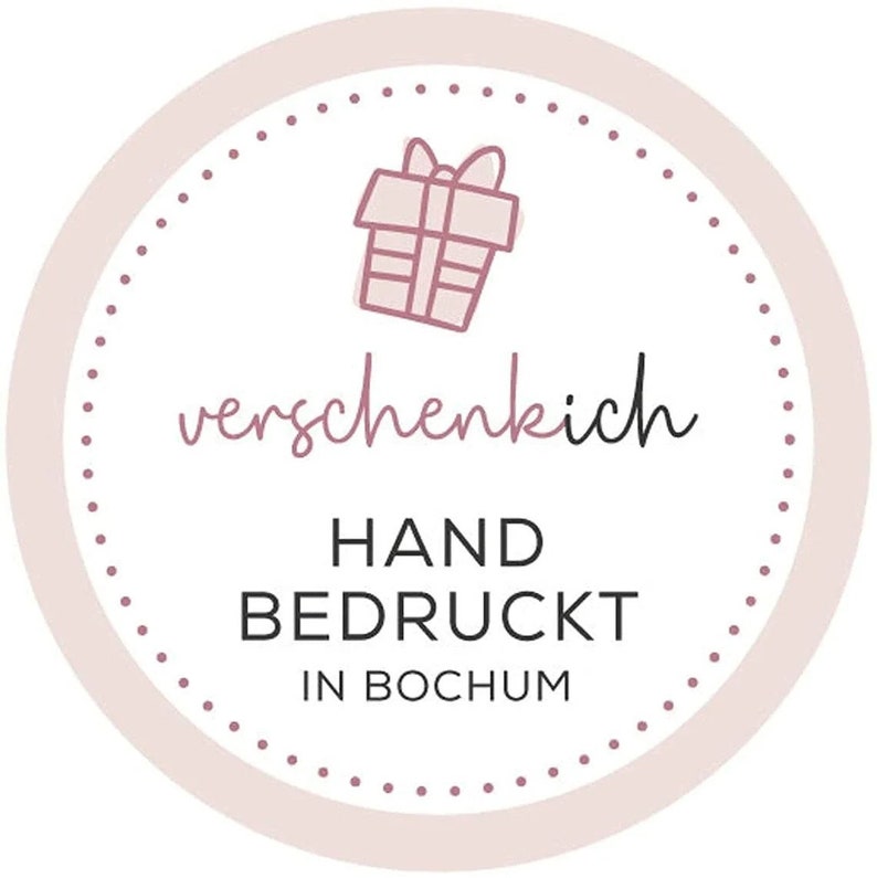 May include: A round, light pink and white sticker with a dotted border. The sticker features a line drawing of a gift box and the text "verschenkich", "HAND BEDRUCKT IN BOCHUM" in a mix of script and block letters.