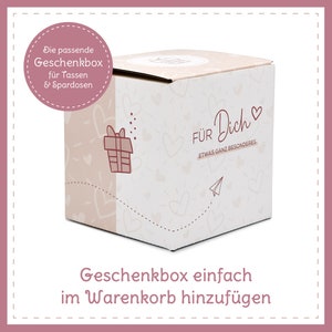 May include: A square gift box with a light pink and white design. The box has the words "F&Uuml;R Dich" and "ETWAS GANZ BESONDERES" printed on it, along with a gift icon, hearts, and a paper airplane. The text "Die passende Geschenkbox f&uuml;r Tassen & Spardosen" is also visible.