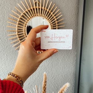 Könnte beinhalten: Ein weißer Geschenkgutschein mit rosa Schrift, auf dem "Etsy Von Herzen" mit einem rosa Herzsymbol und darunter "Geschenkcoupon" steht. Der Text "verschenk dich" steht in kleinerer Schrift am unteren Rand des Gutscheins.