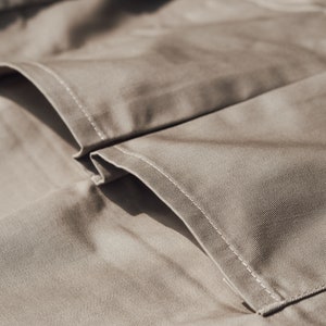 May include: Close-up of tan fabric with visible stitching. The image highlights the texture and construction of the material, showcasing the details of the seams and folds. The neutral color and close perspective suggest a focus on textile craftsmanship.