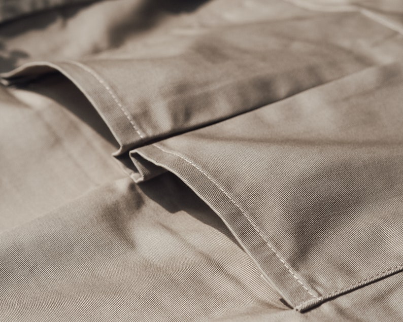 May include: Close-up of tan fabric with visible stitching. The image highlights the texture and construction of the material, showcasing the details of the seams and folds. The neutral color and close perspective suggest a focus on textile craftsmanship.