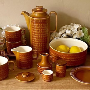 May include: A vintage brown and white patterned tea set with a teapot, creamer, sugar bowl, cups, saucers, and a serving bowl. The set is arranged on a wooden table with lemons in the serving bowl.
