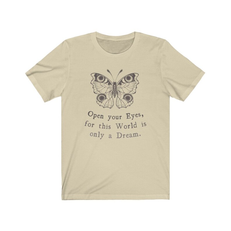 May include: A light beige t-shirt featuring a detailed butterfly illustration in dark brown. Below the butterfly, the text reads, "Open your Eyes, for this World is only a Dream." The shirt has short sleeves and a crew neck.