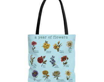 May include: A light blue tote bag with a year of flowers design. The bag features a different flower for each month of the year, with the name of the month and flower printed below each image. The text "a year of flowers" is printed at the top of the bag.