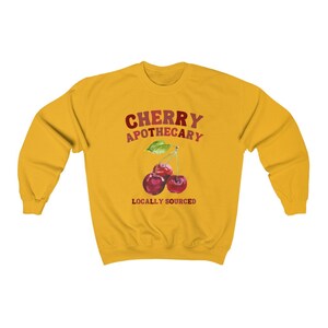 May include: Yellow sweatshirt with the text "CHERRY APOTHECARY" in red and white lettering. Below the text is a graphic of three red cherries with green leaves and the text "LOCALLY SOURCED" in red lettering.