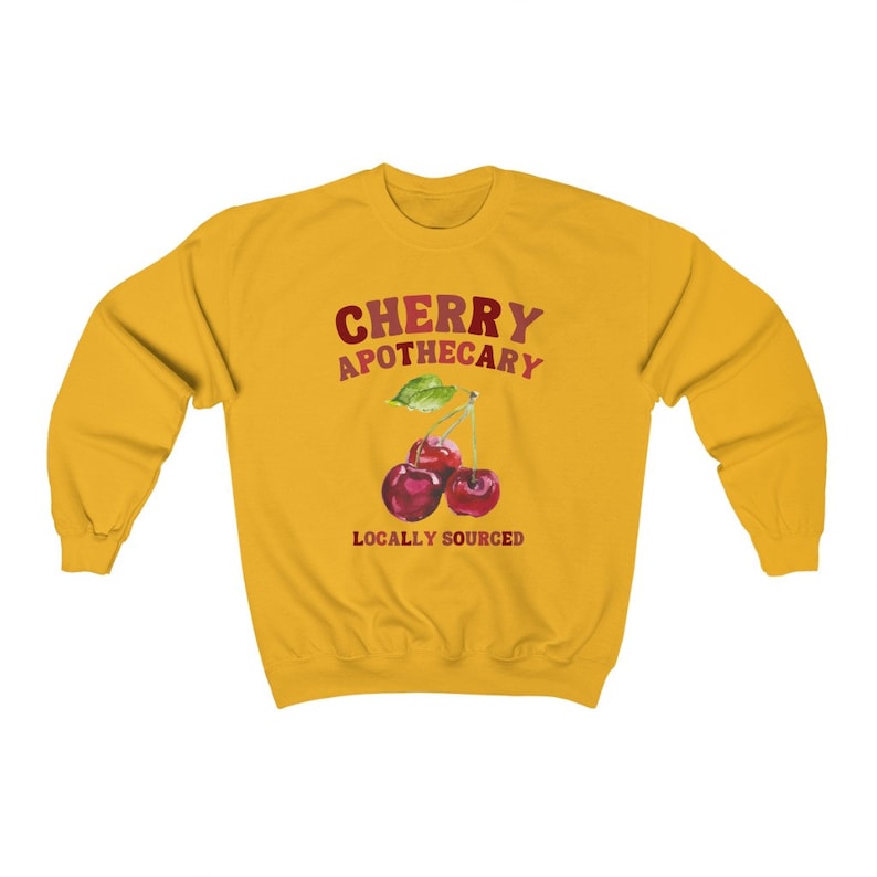 May include: Yellow sweatshirt with the text "CHERRY APOTHECARY" in red and white lettering. Below the text is a graphic of three red cherries with green leaves and the text "LOCALLY SOURCED" in red lettering.