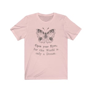 May include: A light pink t-shirt featuring a detailed butterfly illustration in black ink. The butterfly design is above the text "Open your Eyes, for this World is only a Dream."