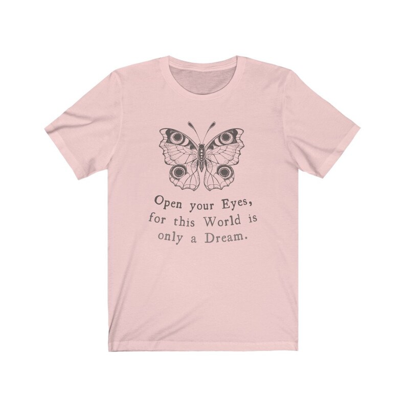 May include: A light pink t-shirt featuring a detailed butterfly illustration in black ink. The butterfly design is above the text "Open your Eyes, for this World is only a Dream."