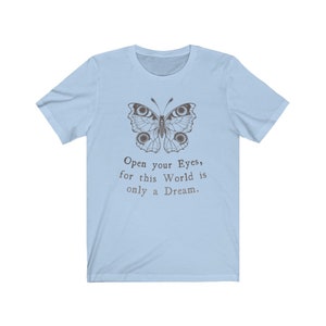 May include: Light blue t-shirt featuring a detailed butterfly illustration in brown tones. The shirt includes the text "Open your Eyes, for this World is only a Dream" in a serif font. The tee has short sleeves and a crew neck.