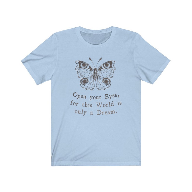 May include: Light blue t-shirt featuring a detailed butterfly illustration in brown tones. The shirt includes the text "Open your Eyes, for this World is only a Dream" in a serif font. The tee has short sleeves and a crew neck.