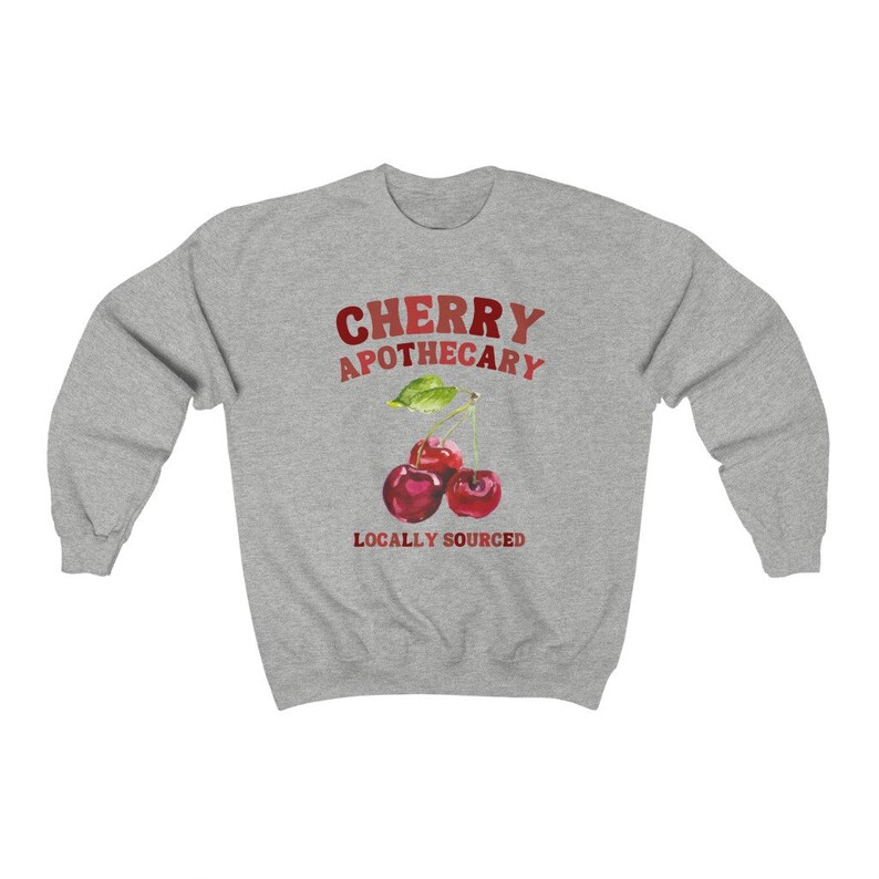 May include: Gray sweatshirt with the text "CHERRY APOTHECARY LOCALLY SOURCED" in red and white. A watercolor illustration of three red cherries with green leaves is centered on the sweatshirt.