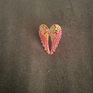 K&ouml;nnte beinhalten: Ein Paar rosa Engelsfl&uuml;gel mit goldenen Verzierungen und bunten Strasssteinen.