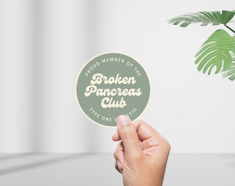 以下が含まれることがあります： 白い文字で「Proud Member of the Broken Pancreas Club Type One Diabetic」と書かれた緑色の丸いステッカーです。