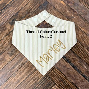May include: Cream-colored striped pet bandana with the name "Marley" embroidered in caramel-colored thread. The bandana has a snap closure and the text "Thread Color: Caramel Font: 2".