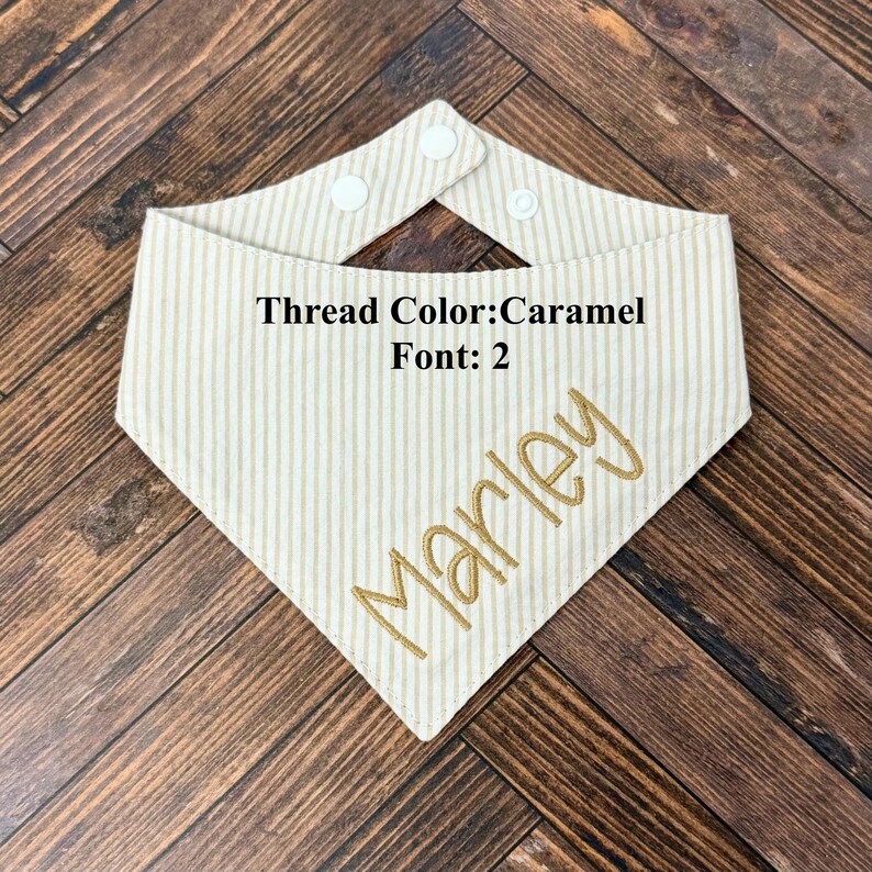 May include: Cream-colored striped pet bandana with the name "Marley" embroidered in caramel-colored thread. The bandana has a snap closure and the text "Thread Color: Caramel Font: 2".