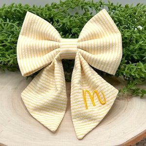 May include: A yellow and white striped bow tie with a yellow embroidered letter "M" on the front.