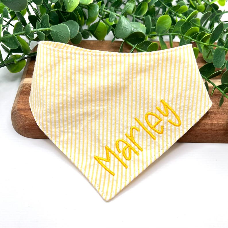 以下が含まれることがあります： 黄色と白のストライプの bandana に、黄色い糸で「Marley」という名前が刺繍されています。