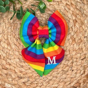 May include: Rainbow striped fabric bow with a white letter M embroidered on it.