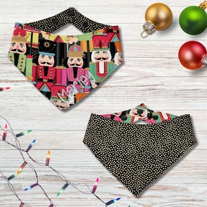May include: Reversible dog bandana featuring a colorful nutcracker print on one side and a black polka dot pattern on the other. The name "Marley" is embroidered on the nutcracker side. The bandana is designed to be worn around a dog's neck.