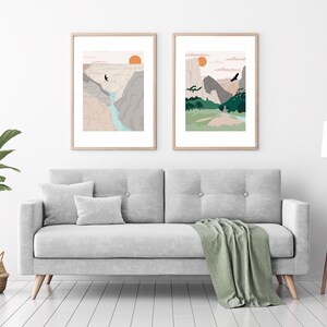 May include: Two framed illustrations of mountain landscapes with a sunset in the background. The illustrations are in a minimalist style with muted colors and simple lines. The illustrations are hung on a white wall above a gray sofa.