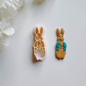 May include: A white plastic cookie cutter shaped like a rabbit, and a brown and blue fondant rabbit.