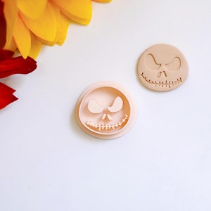 Puede incluir: Dos cortadores de galletas de plástico marrón claro con forma de la cara de Jack Skellington de la película Pesadilla antes de Navidad.