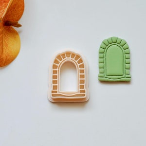May include: Two cookie cutters, one in white plastic and one in green plastic, shaped like arched doorways.