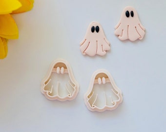 May include: Four pink ghost-shaped cookie cutters, two with black eyes. The cutters are on a white surface.