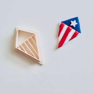 May include: A white plastic cookie cutter shaped like a diamond kite with a red, white, and blue fondant kite with a white star.
