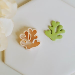 May include: Two cookie cutters, one in the shape of a green seaweed and the other in the shape of a peach-coloured coral.