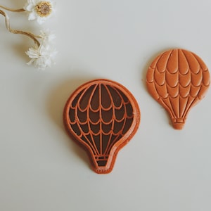 May include: Two brown clay cookie cutters shaped like hot air balloons. One cutter is solid and the other is an outline.