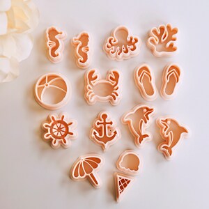 May include: A set of 12 plastic cookie cutters in various shapes, including a seahorse, octopus, crab, anchor, dolphin, beach ball, flip flops, ice cream cone, umbrella, and starfish. The cutters are all a light peach colour.