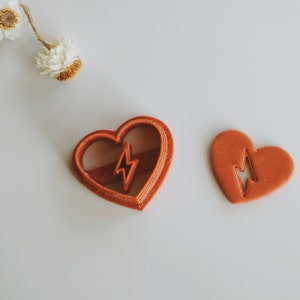 May include: Two heart-shaped cookie cutters, one with a lightning bolt design inside. Both are a reddish-brown color.