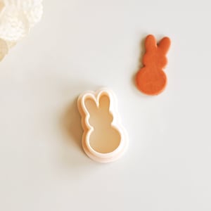 May include: A white plastic cookie cutter shaped like a bunny rabbit. The cutter has a raised design and is used to cut out shapes from cookie dough.