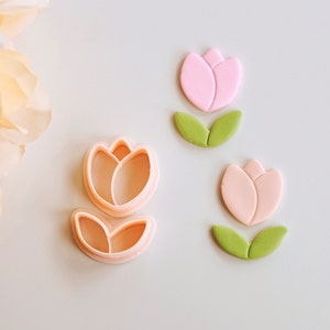 May include: Three cookie cutters in the shape of tulips. The cutters are made of pink and green plastic. The cutters are on a white background.
