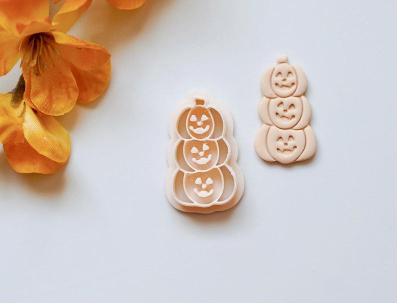 Puede incluir: Dos cortadores de galletas de pl&aacute;stico con forma de pilas de tres calabazas. Los cortadores son de color beige y tienen un acabado liso.